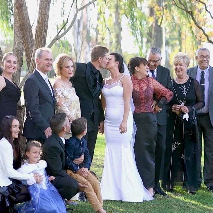 Bride and groom kissing during a family group photo at their wedding