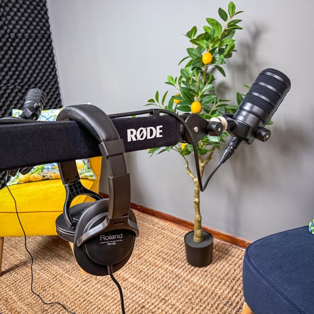 Close-up of a RODE podcast microphone on a boom arm with Roland monitor headphones