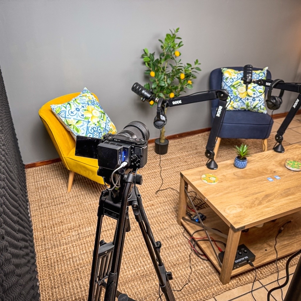 Camera on a tripod filming the two-seat podcast setup at 3-Axis Studios